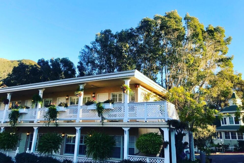 A two-story building with a white balcony and columns, surrounded by trees and a clear blue sky.