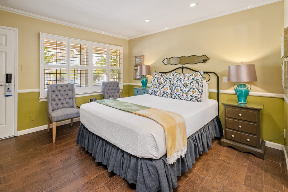 A wide view of a guest room with a bed, nightstand, chair, and window.